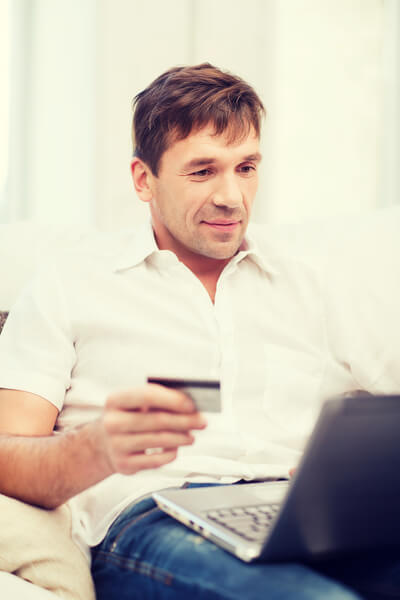 Mann sitzt mit einer Kreditkarte vor dem Laptop